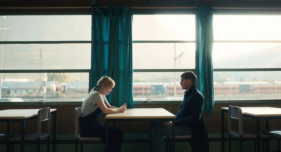 Bastien Bouillon et une jeune femme pleurant autour d'une table de cantine avec vue sur l'extérieur.