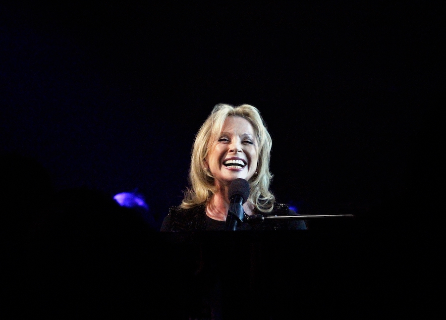 Véronique Sason sur scène large sourire derrière son piano et son micro.