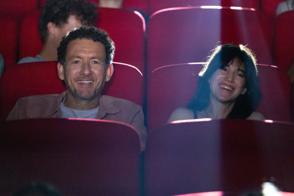 Dany Boon et Charlotte Gainsbourg rient devant un film au cinéma fauteuils rouges.