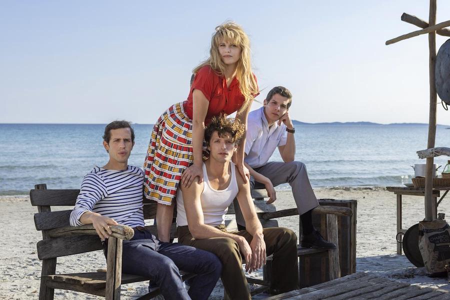 Bardot à la plage debout sur un banc avec ses 3 hommes chemise et maillot marin.