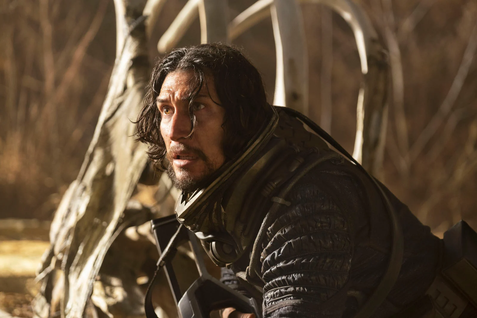 Adam Driver apeuré avec une arme devant une carcasse de dinosaure.