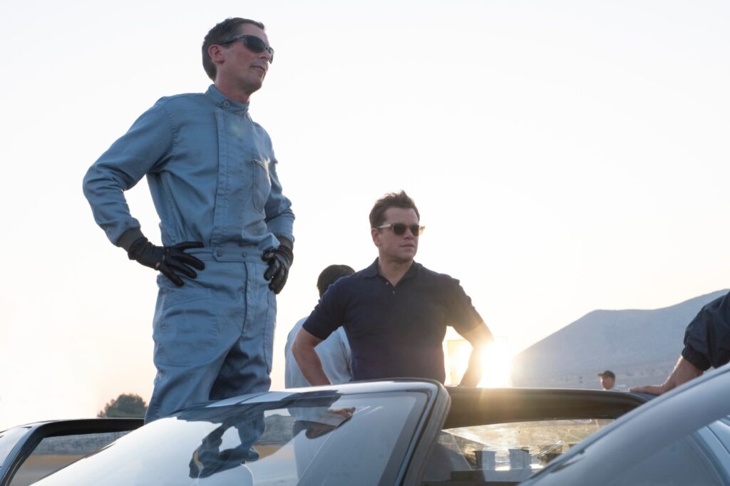 Christian Bale et Matt Damon contrejour au soleil devant une voiture de course.