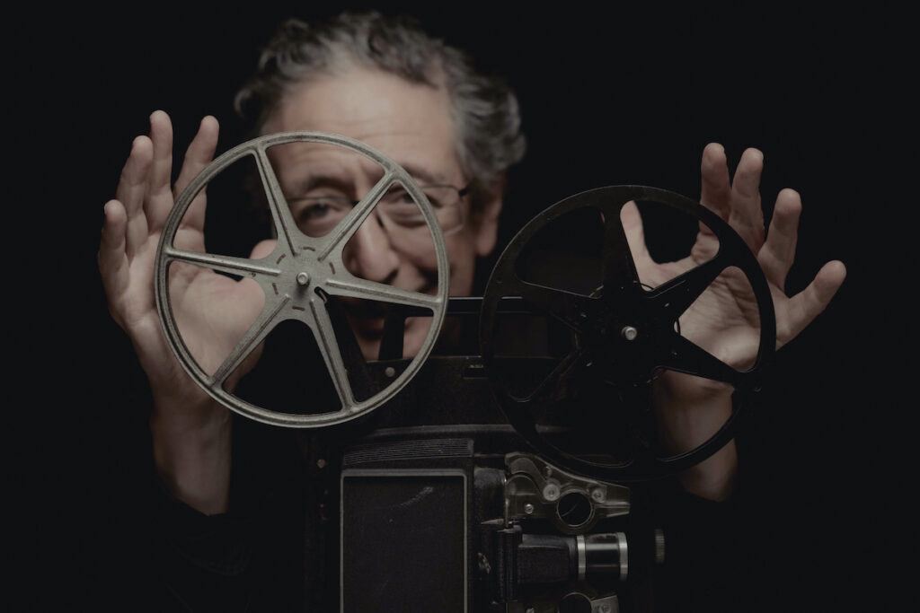 Jean-Marc Luisada mains en l'air derrière un projecteur de films.