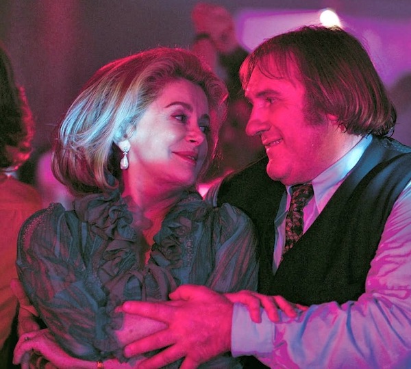 Deneuve et Depardieu sourient et dansent sous la lumière violette d'une boîte de nuit.